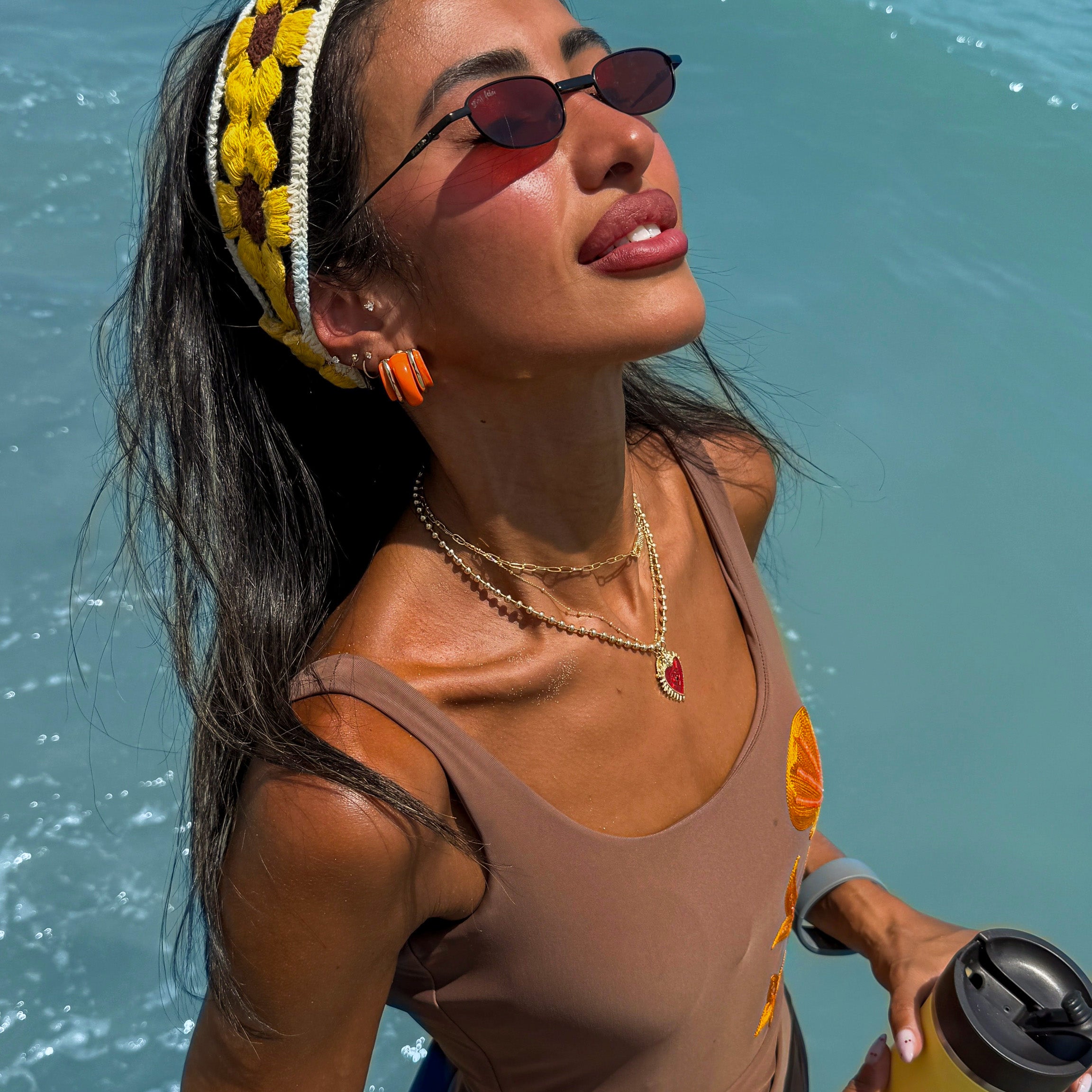 Woman in sunglasses and tank top holding a drink by the water