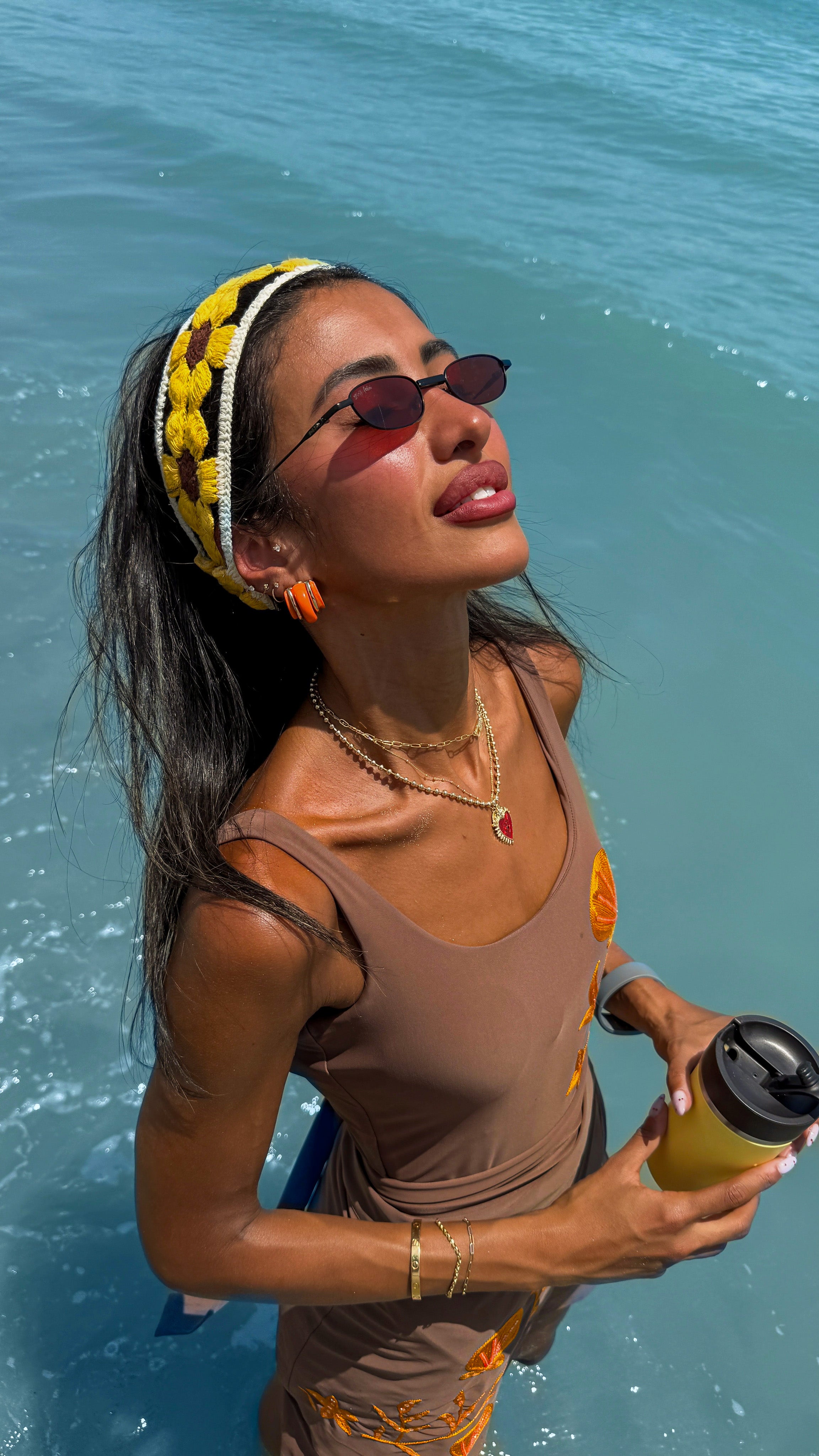Woman in sunglasses and tank top holding a drink by the water