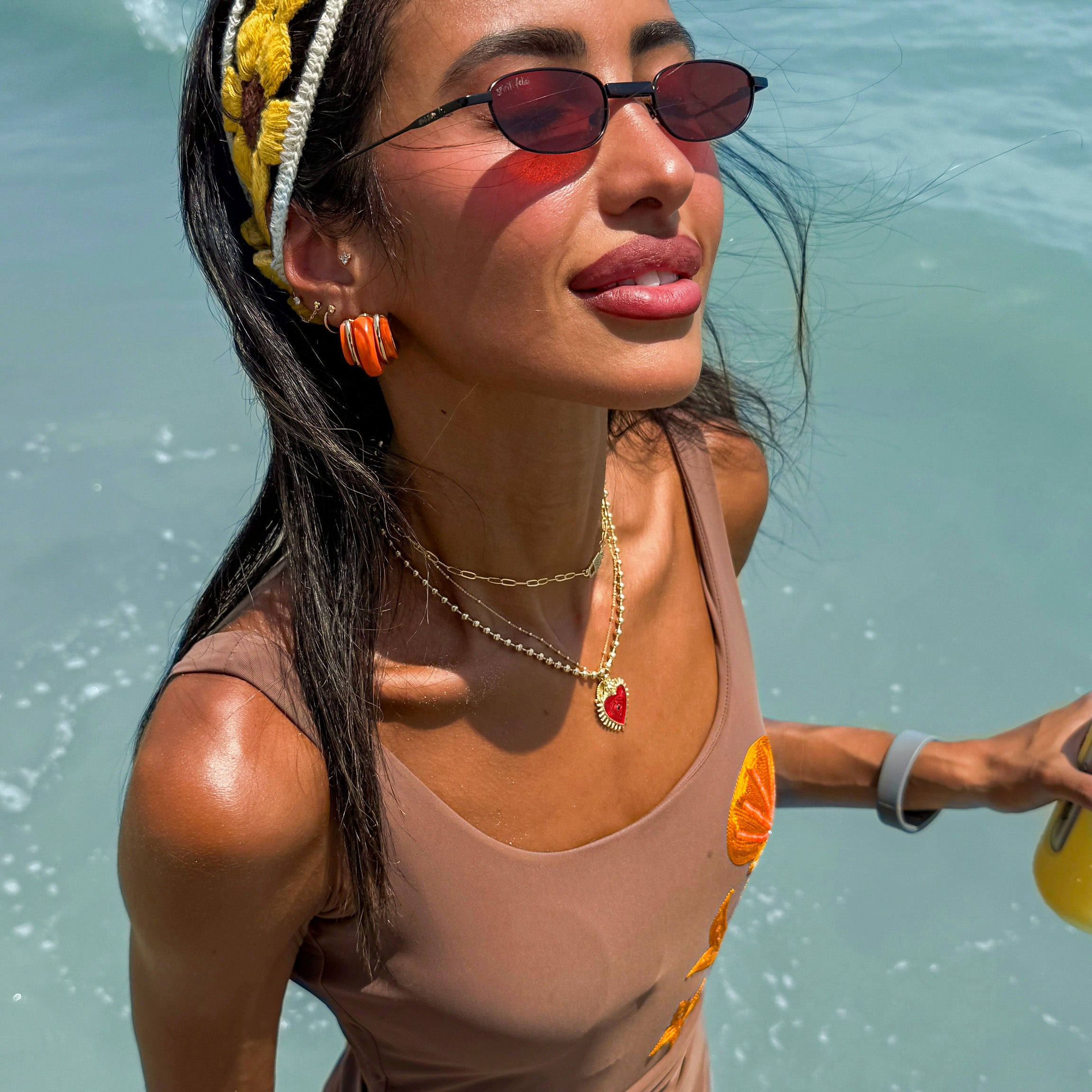 Woman in a swimsuit with sunglasses and a headband, standing in water.