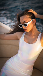 Woman wearing a white tank top and sunglasses by the water