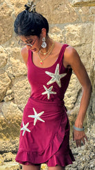 Woman wearing a red dress with starfish patterns against a stone wall.
