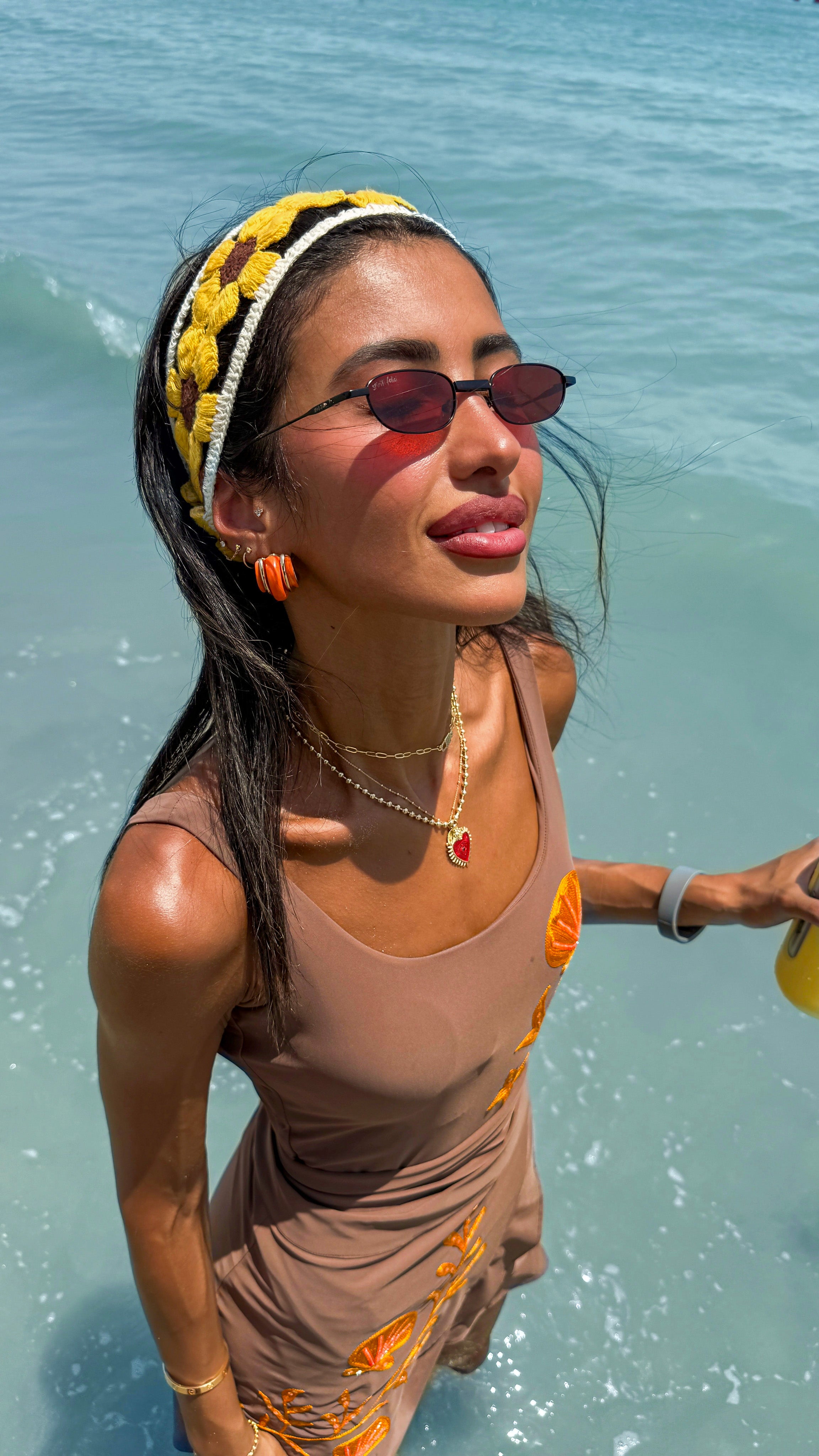 Woman in a swimsuit with sunglasses and a headband, standing in water.